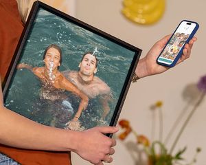 Een vrouw houdt albelli wanddecoratie vast met daarop een gezin dat in het water speelt op vakantie, als inspiratie om vakantiefoto’s om te zetten in prachtige wanddecoratie.