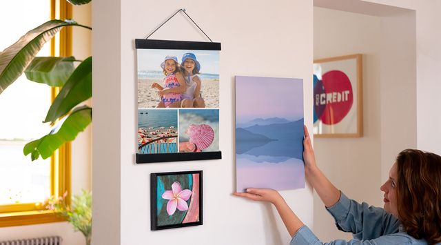 Iemand hangt een fotoafdruk naast twee ingelijste fotoafdrukken.